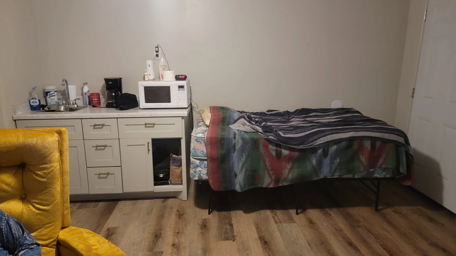 A furnished room shared by Bridging the Gaps, with a bed, armchair, and kitchen essentials